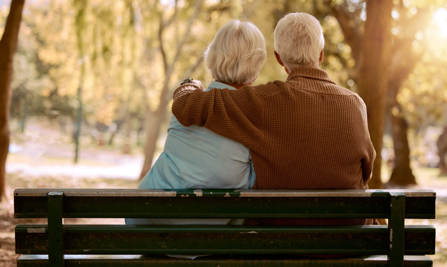 Senior man holds senior woman on park bench on a peaceful day.