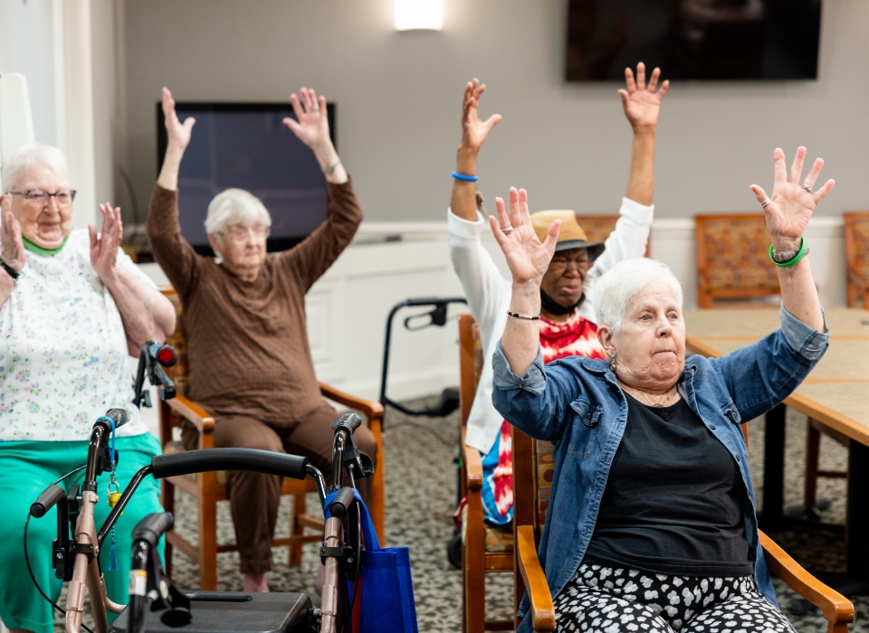 Senior residents raising arms during group exercise session in a community room.