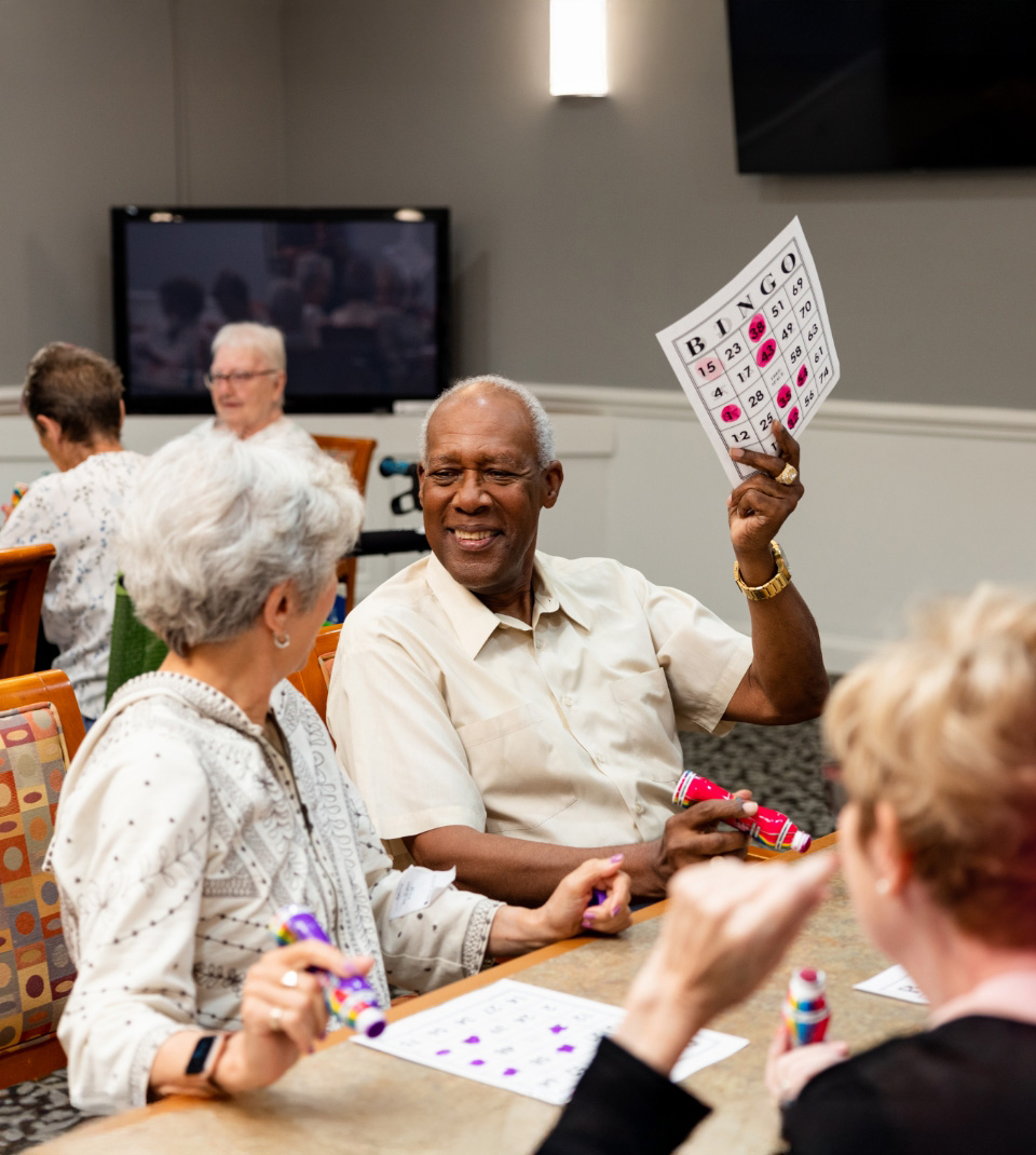 Residents enjoying a bingo game in a community room with lively interaction.
