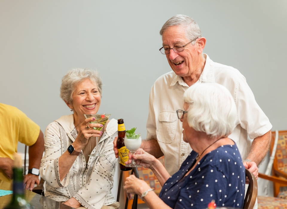 Three smiling seniors enjoying drinks together at a social event in a communal area.
