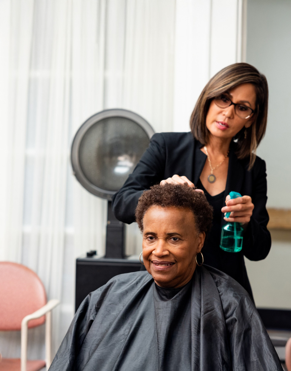 Hairdresser styling a senior womans hair with a spray bottle in a salon setting.