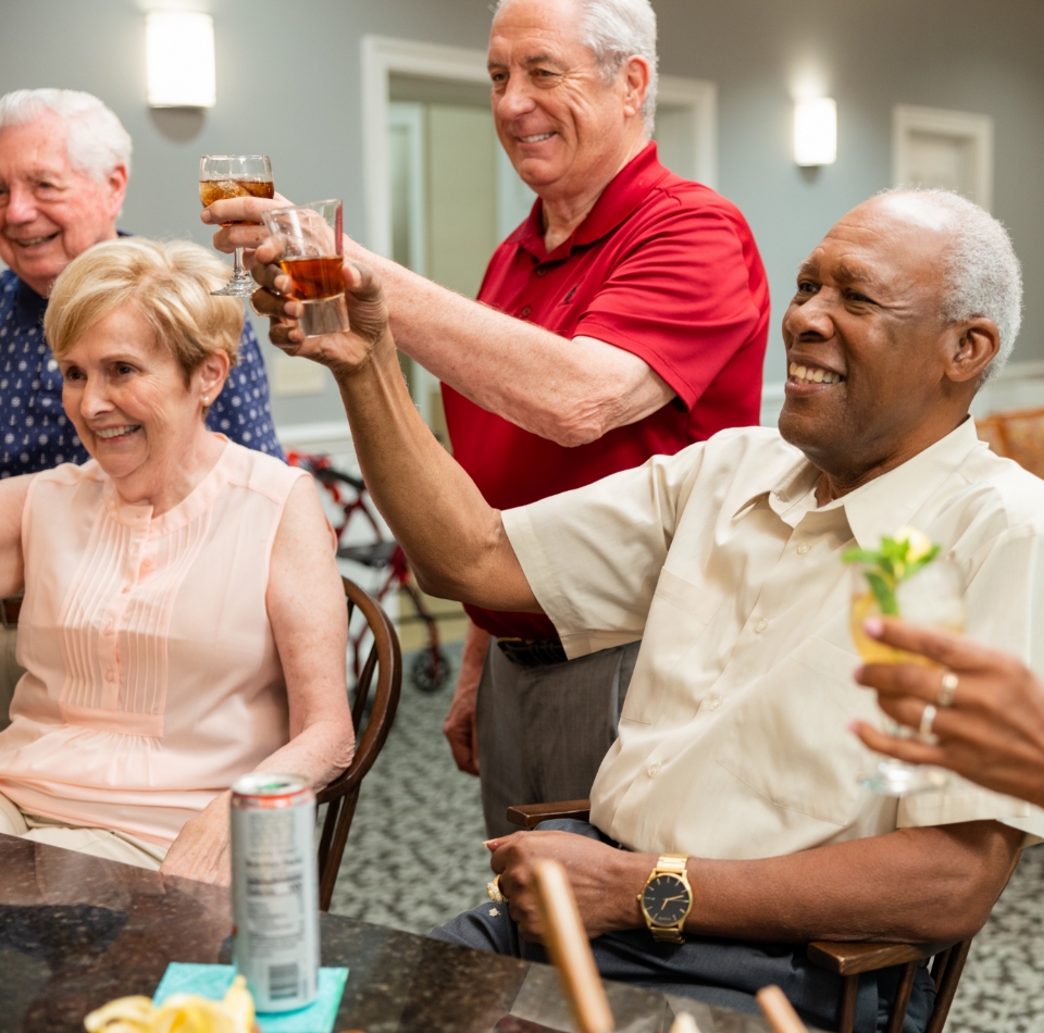 Group of seniors raising glasses in a bright communal dining area.